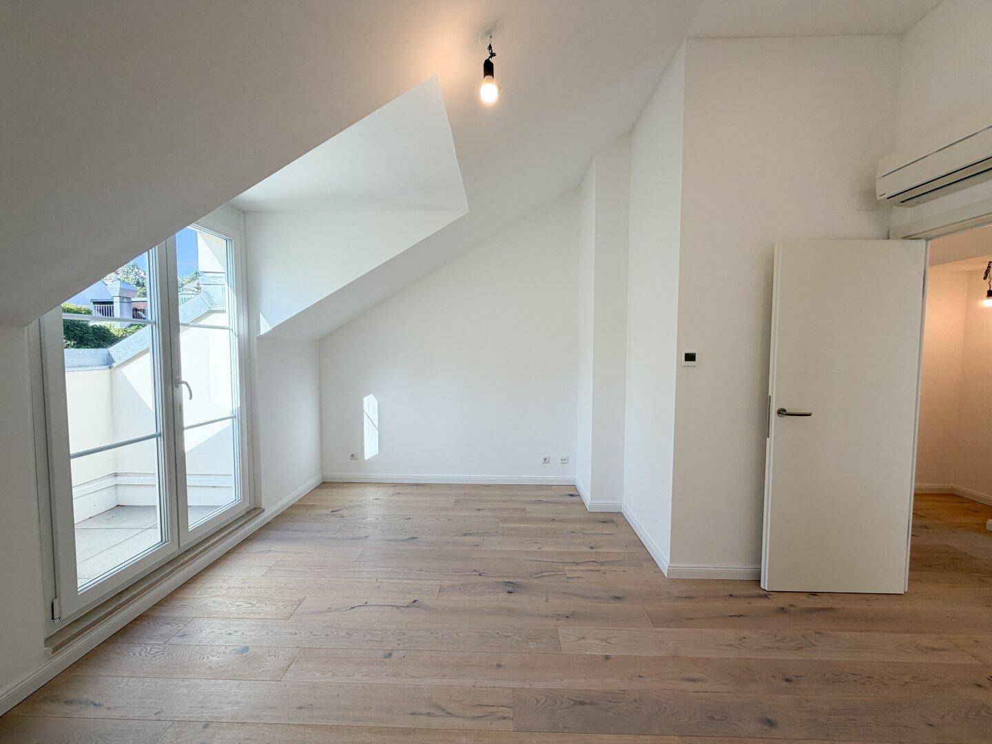 Helles Schlafzimmer mit Holzboden, schrägen Decken und kleinem Balkon.