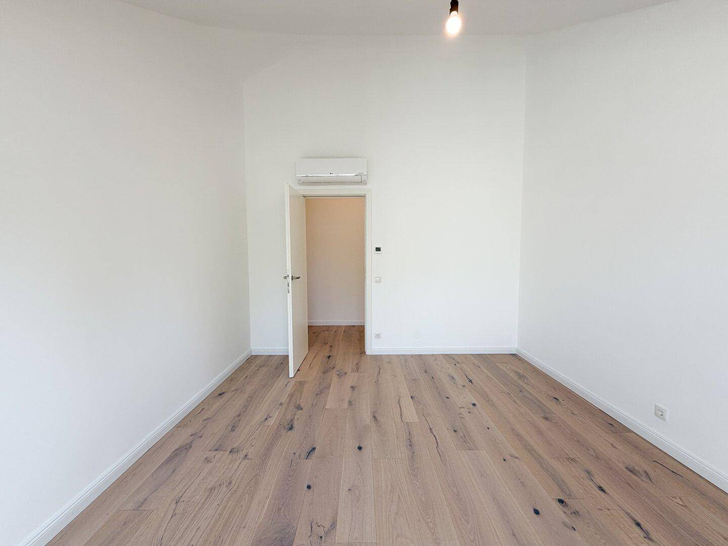 Geräumiges Zimmer mit Holzboden, Klimaanlage und offenem Zugang zu einem weiteren Raum.
