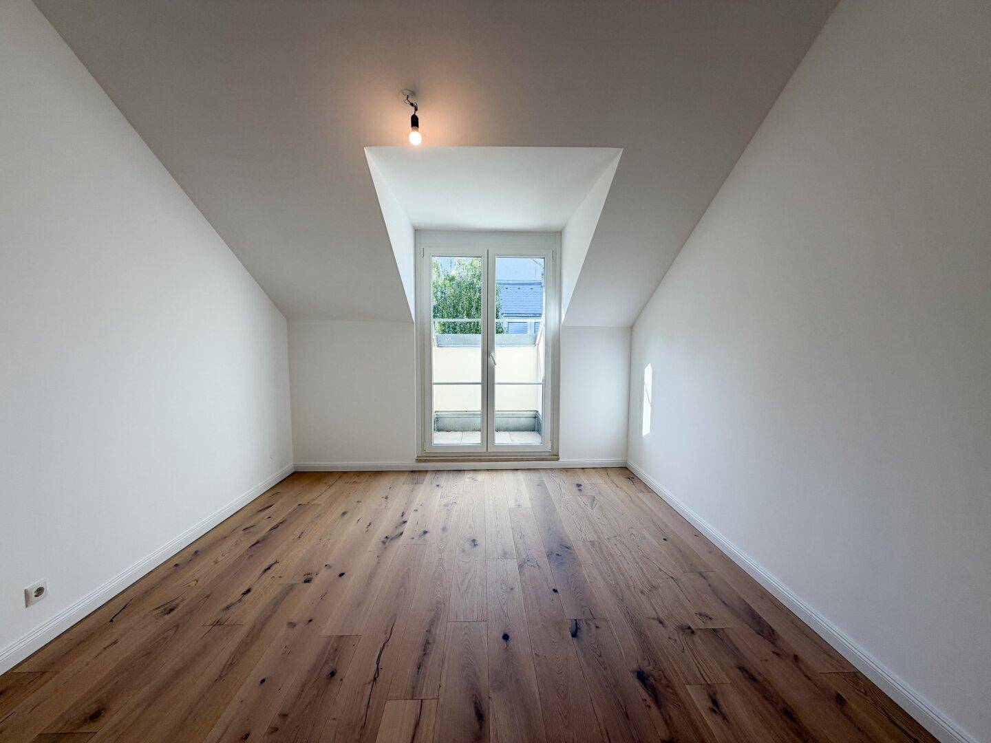 Helles Schlafzimmer mit Holzboden, schrägen Decken und französischem Balkon.