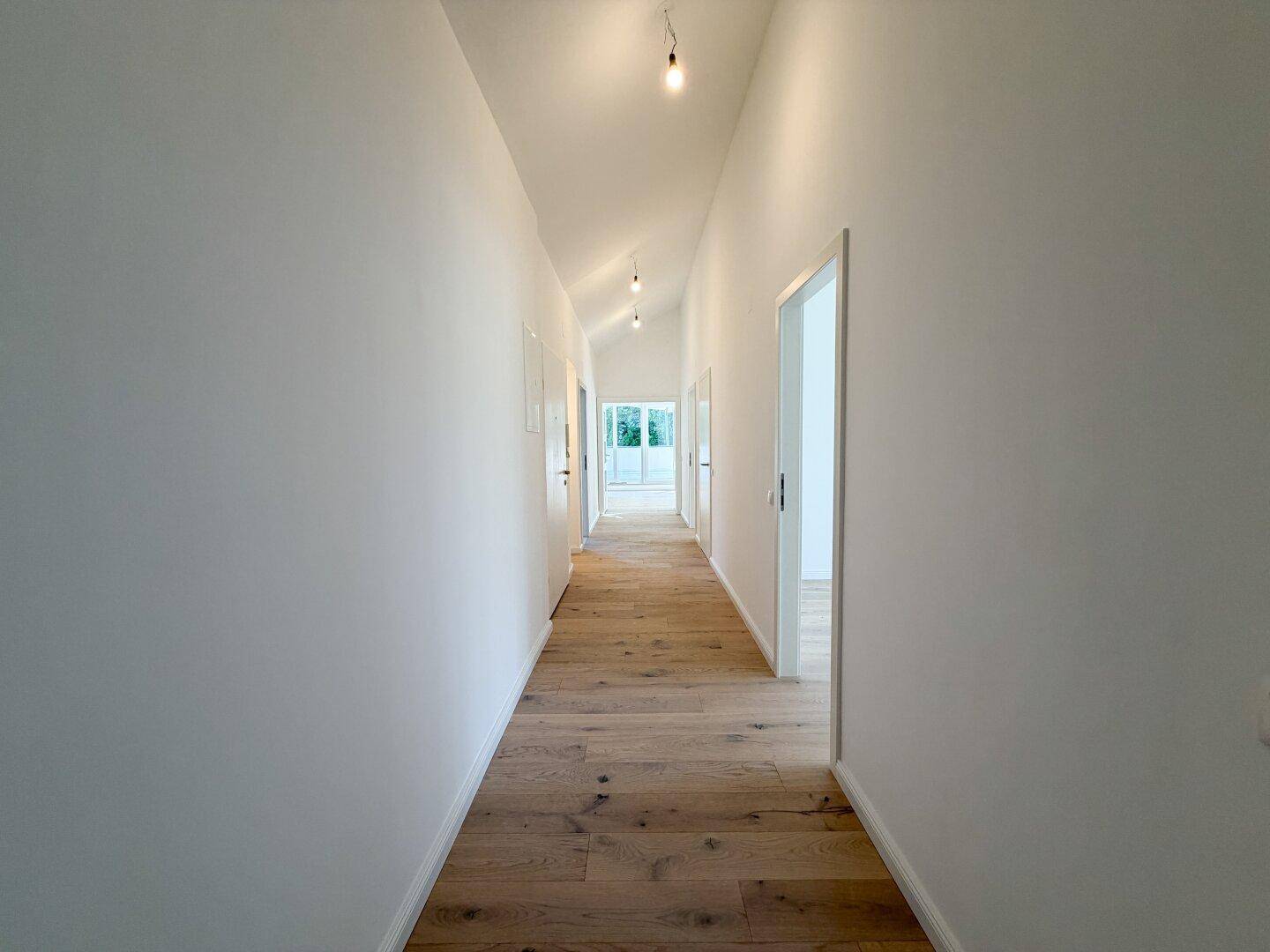 Langer, heller Flur mit Holzboden und weißen Wänden, der zu weiteren Räumen führt.