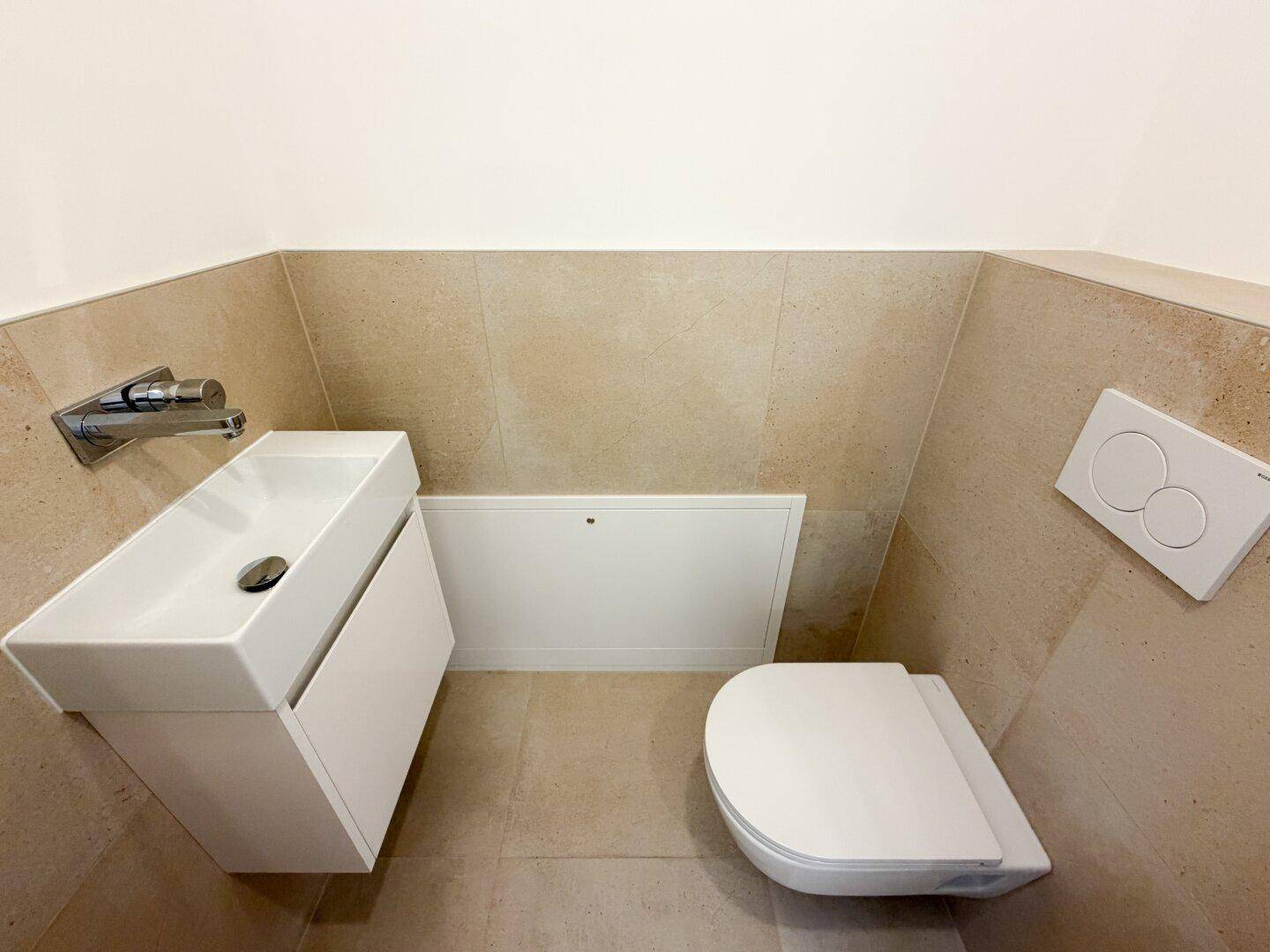 Modernes Gäste-WC mit wandhängender Toilette und kleinem Waschbecken in neutralen Farbtönen.