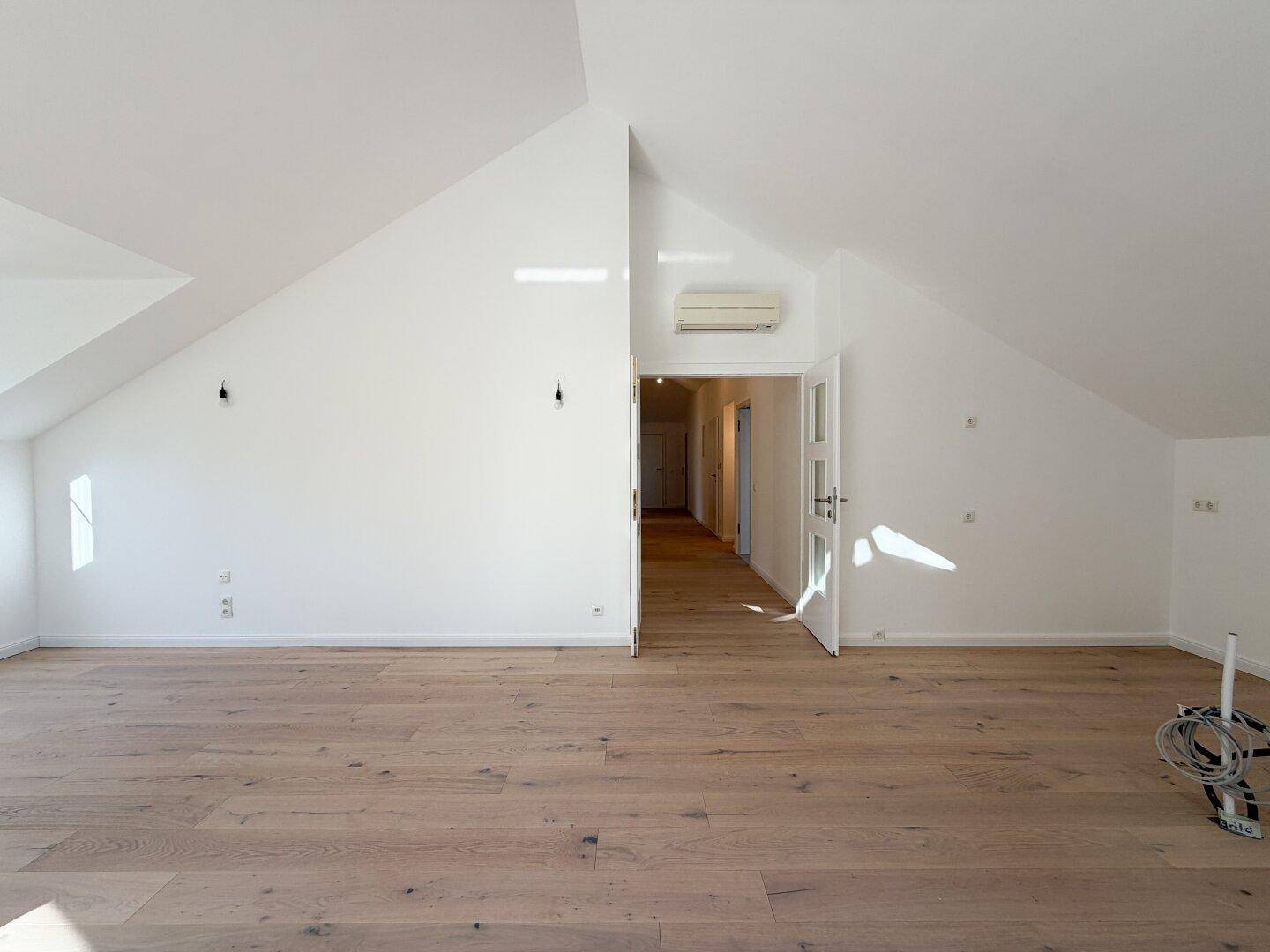 Großer Wohnbereich mit Holzboden, Klimaanlage und offenem Zugang zum Flur.