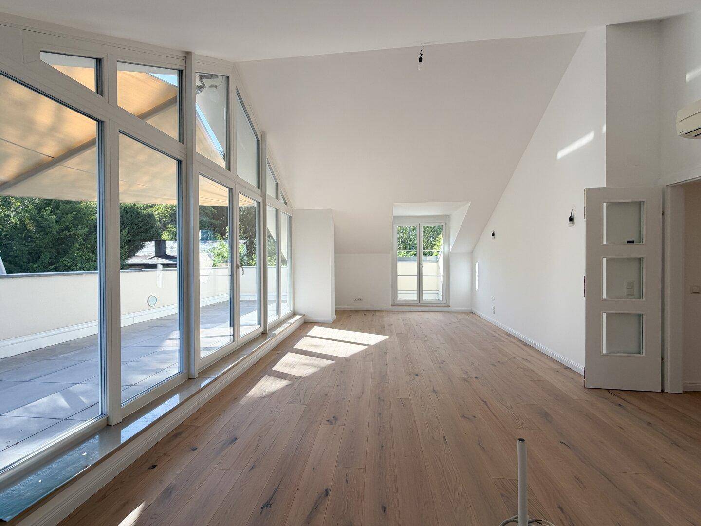 Geräumiger Wohnbereich mit schrägen Decken, Holzboden und weitem Blick durch die Fensterfront.