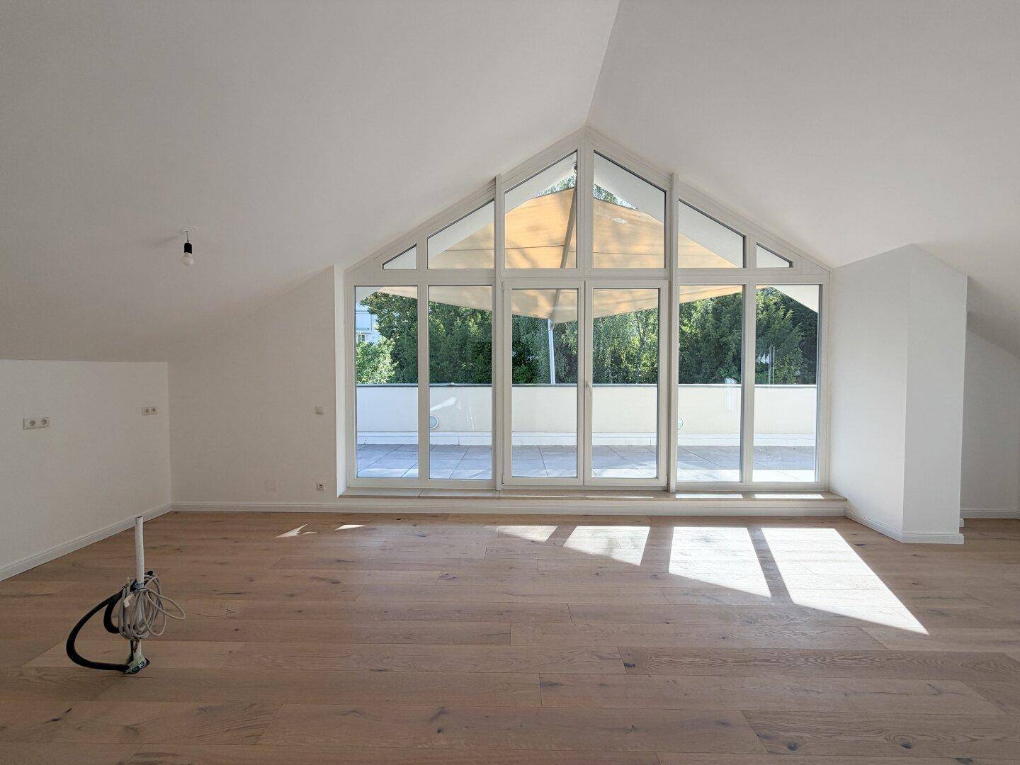 Lichtdurchfluteter Wohnraum mit Holzboden und Panoramafenstern, die den Blick ins Grüne öffnen.