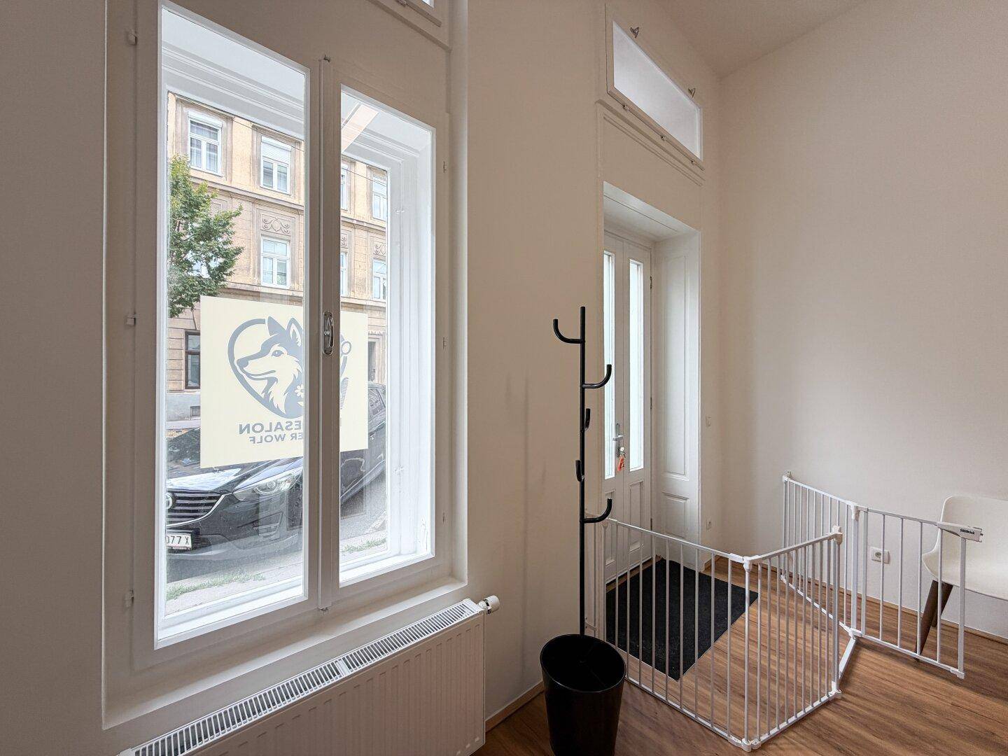 Detailansicht der hohen Fenster und der Eingangstür mit einem Kleiderständer und einem Welpengitter.