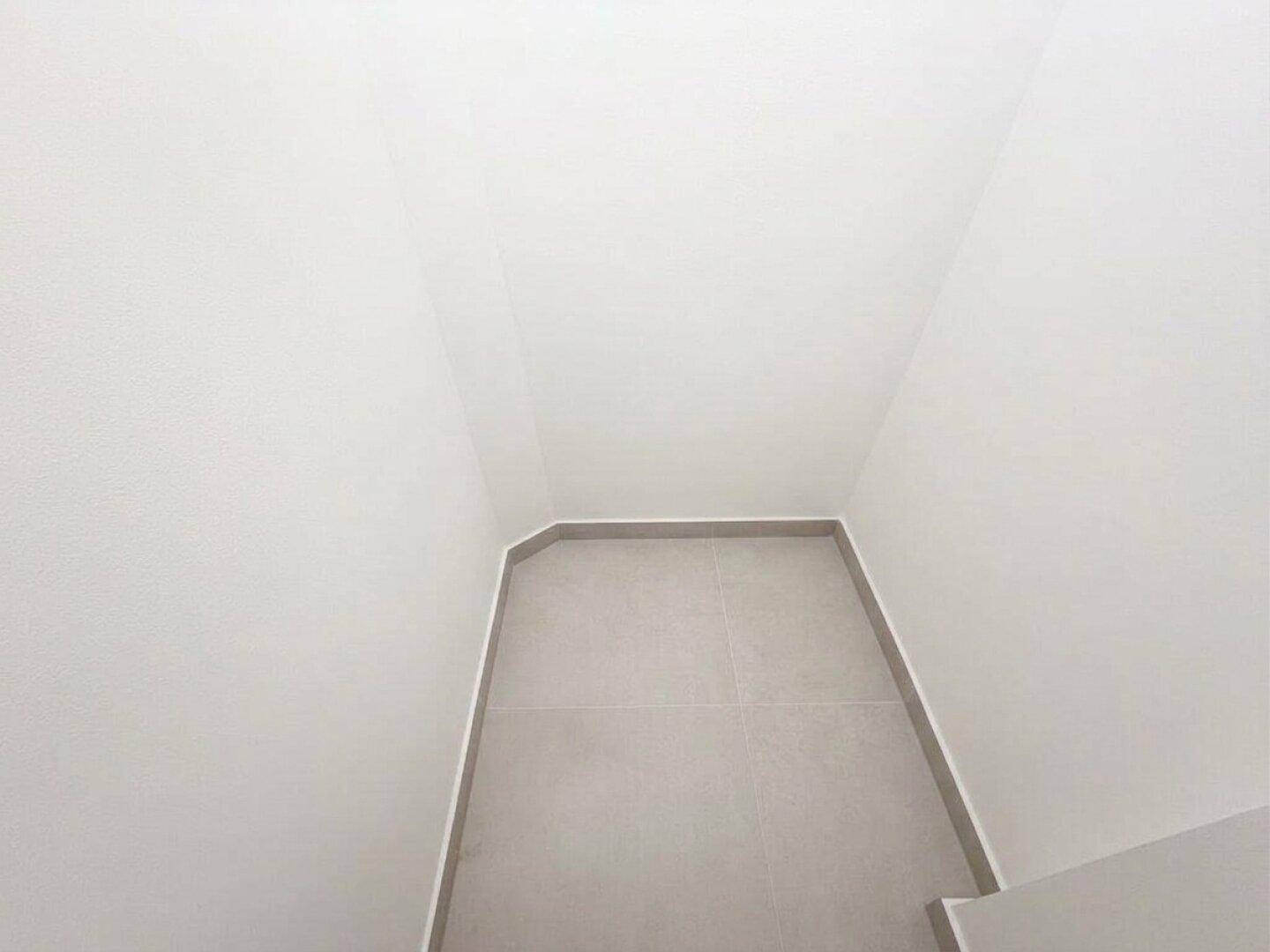 Blick auf den gefliesten Boden und die weißen Wände eines kleinen, sauberen Toilettenraums.