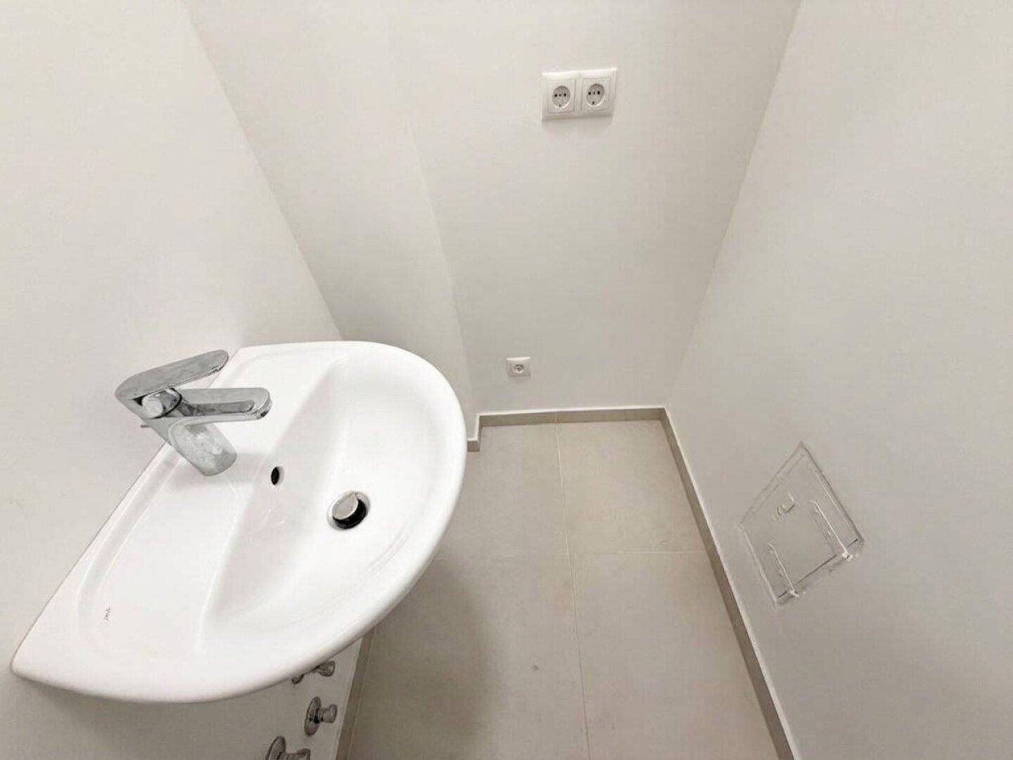 Kleiner Toilettenraum mit Waschbecken und Steckdosen, hell gefliest und weiß gestrichen.