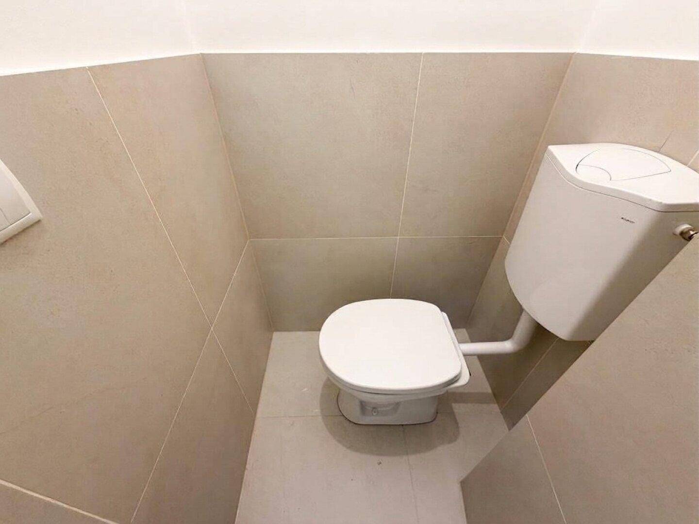 Kleiner Toilettenraum mit beigefarbenen Fliesen an Wänden und Boden, ausgestattet mit einer Toilette.