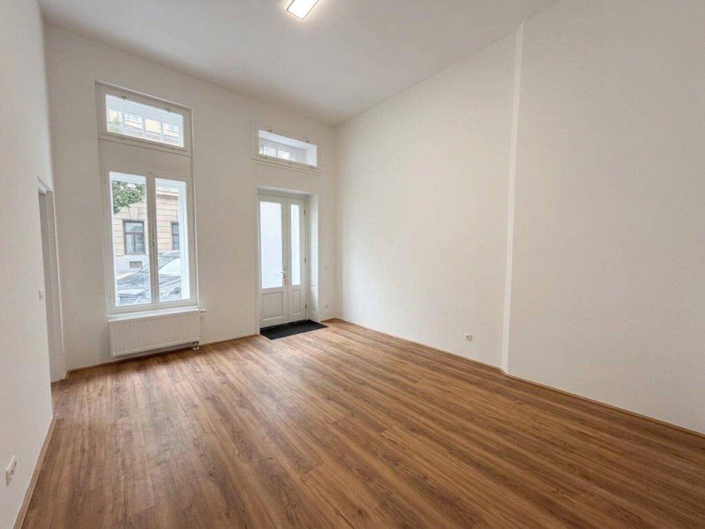 Geräumiger, heller Raum mit Laminatboden und hohen Fenstern, bereit zur individuellen Gestaltung.
