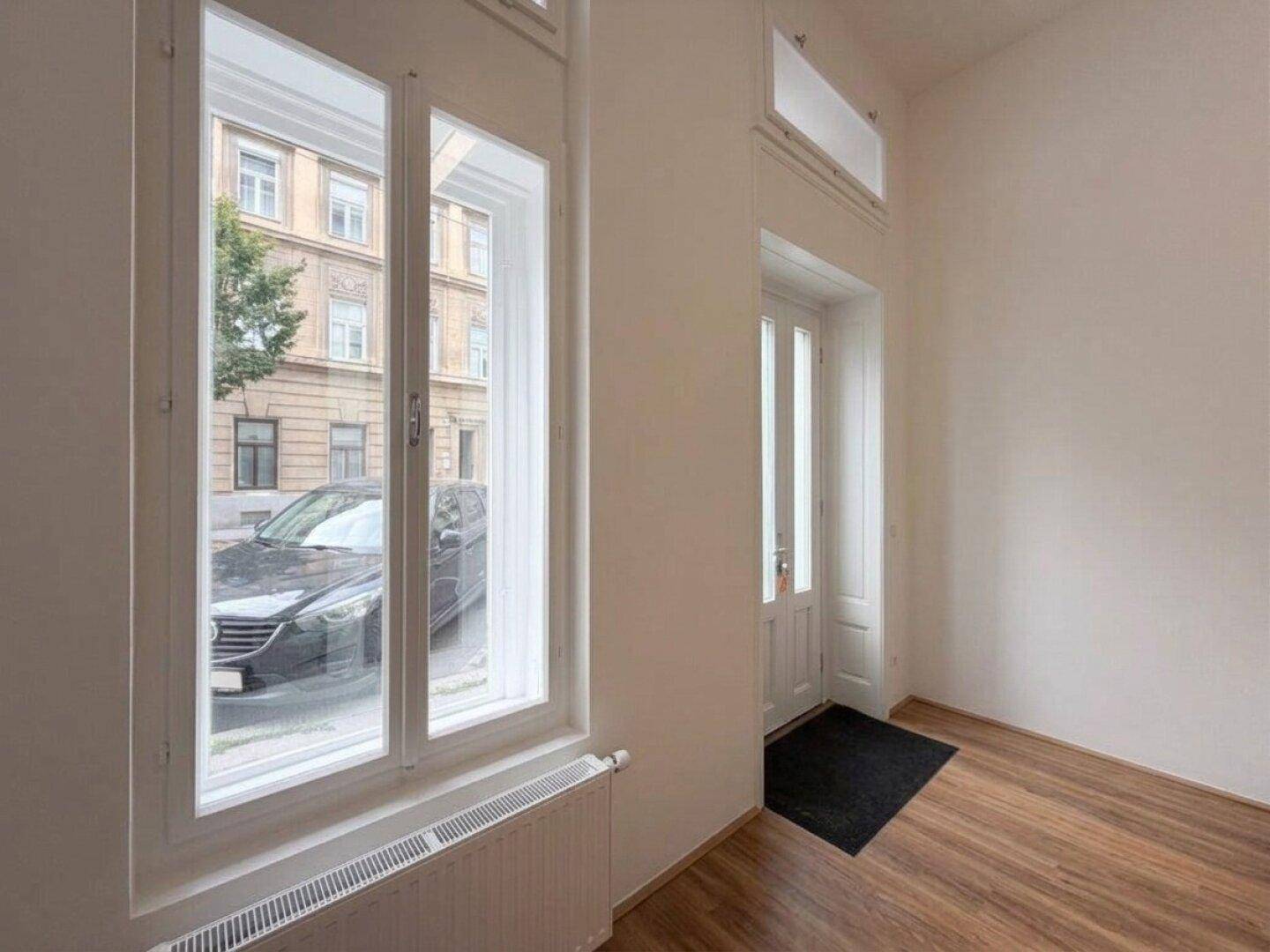 Detailansicht der hohen Fenster und der Eingangstür mit Blick auf die Straße und parkende Autos.