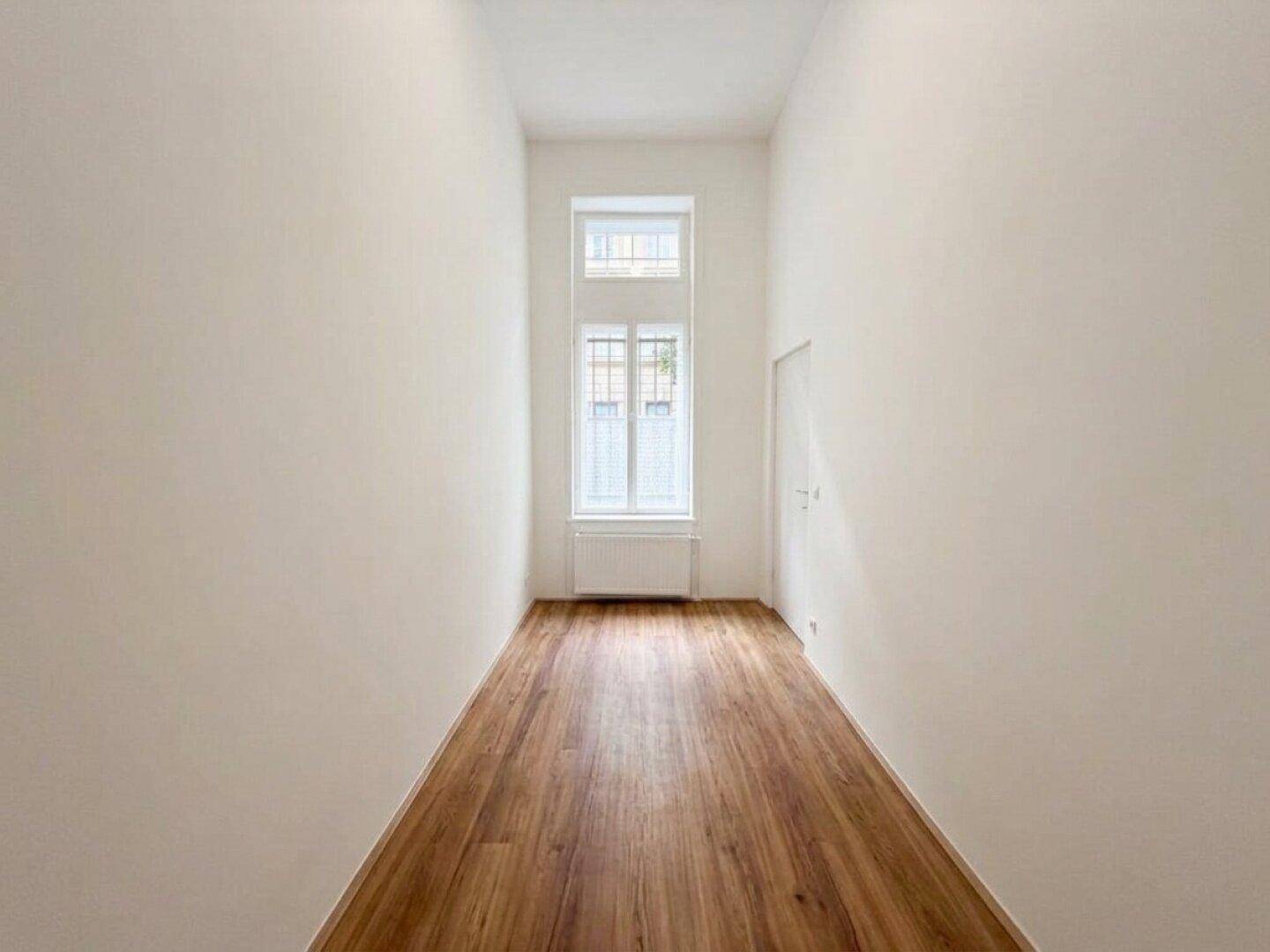 Schmaler, langer Raum mit hohen Decken und einem Fenster am Ende, ideal als Flur oder Durchgang.