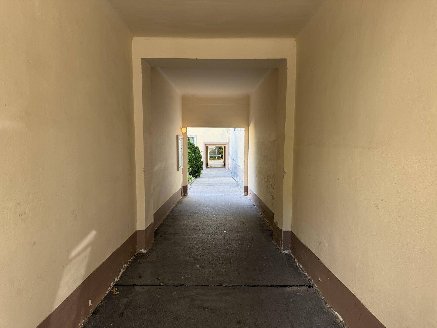 Heller Durchgang mit Blick auf einen grünen Innenhof am Ende.