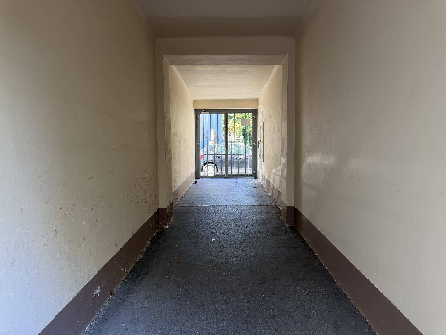 Langer Durchgang mit Gittertür, der zu einem Innenhof führt.