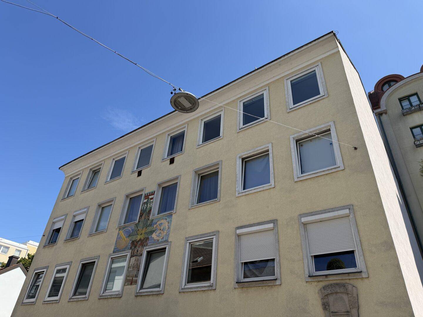 Fassade eines Mehrfamilienhauses mit vielen Fenstern und Rollläden unter blauem Himmel.
