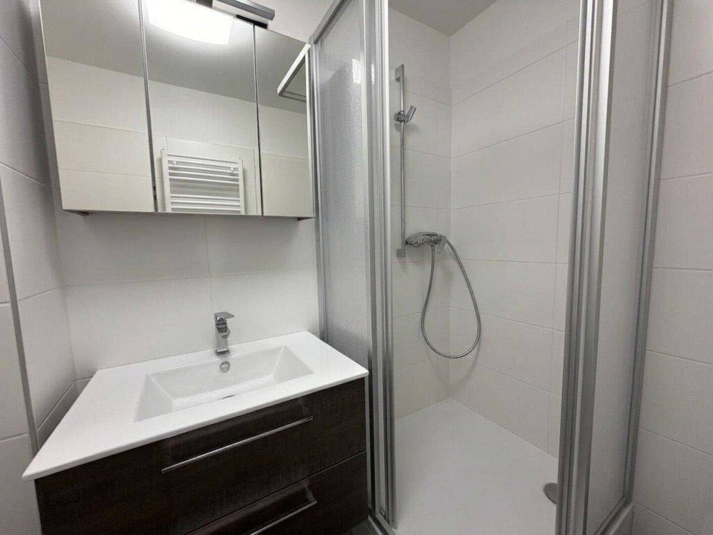 Helles Badezimmer mit weißen Fliesen, modernem Waschbecken und Duschkabine.