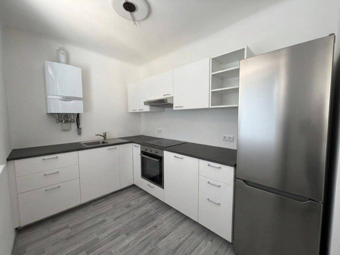 Moderne Küche mit weißen Schränken, dunkler Arbeitsplatte und Edelstahlkühlschrank.