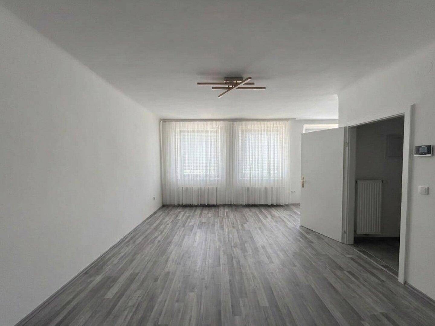 Heller, leerer Raum mit modernem grauem Laminatboden und zwei Fenstern.