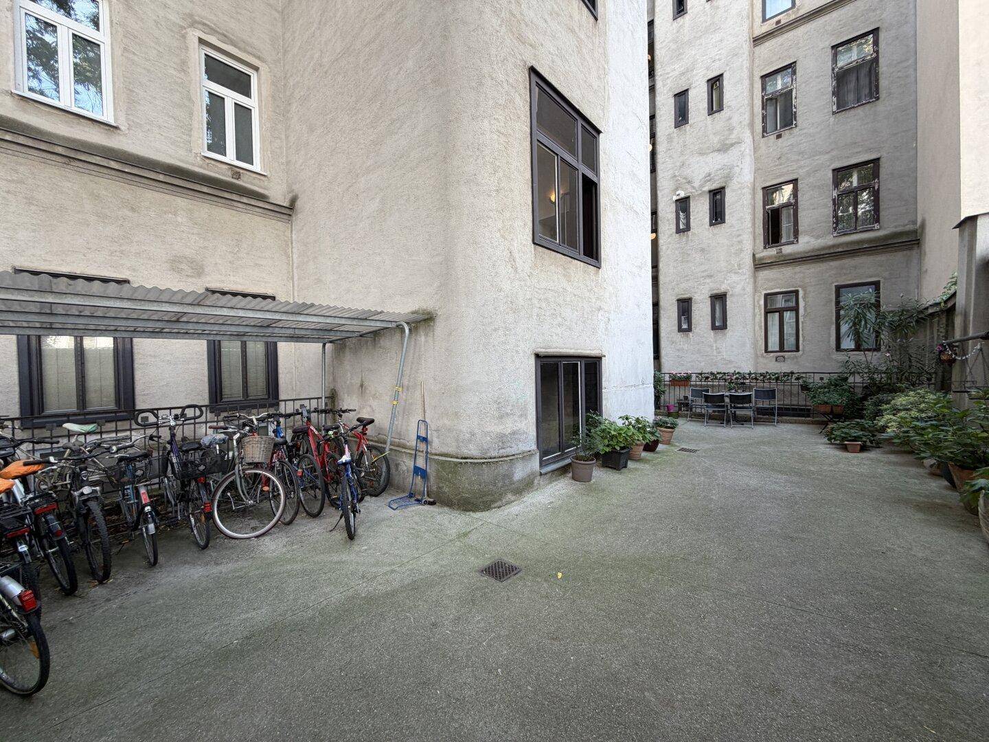 Innenhof mit Fahrradabstellplatz und Topfpflanzen, umgeben von Altbaufassaden.