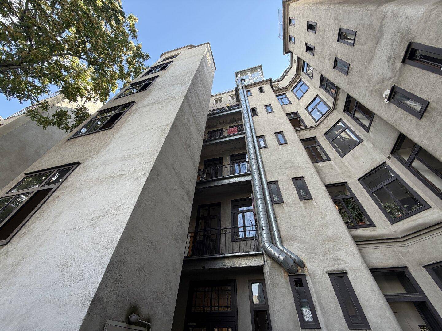 Rückseite eines Altbaus mit vielen Fenstern und einem langen Abflussrohr an der Fassade.
