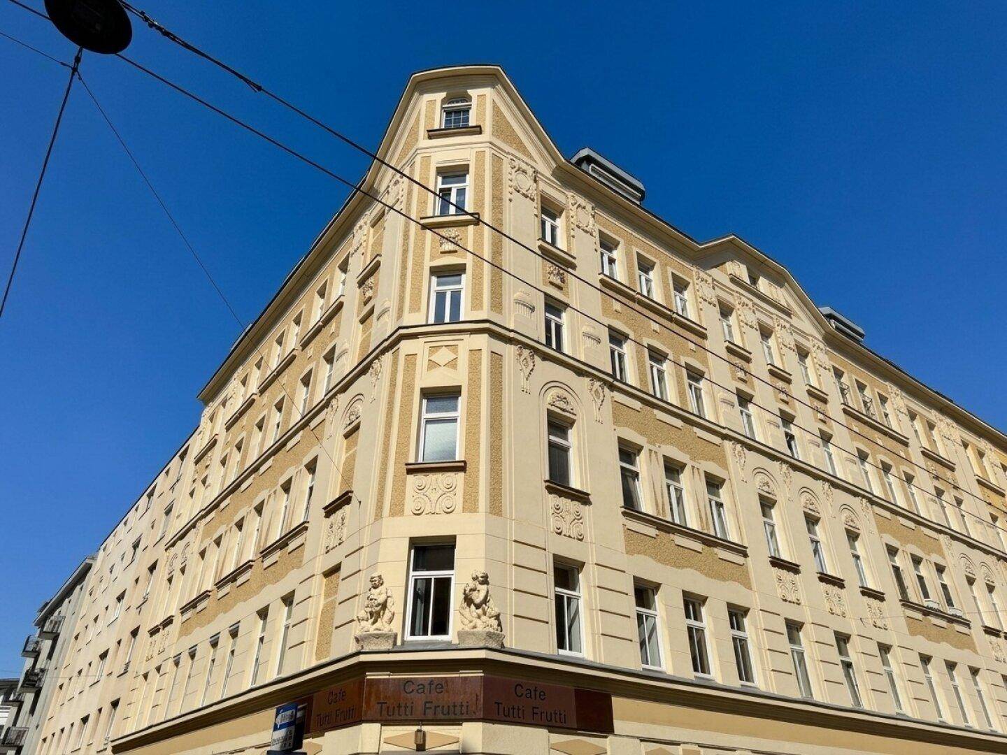 Historisches Eckgebäude mit reich verzierten Fassaden und vielen Fenstern unter blauem Himmel.