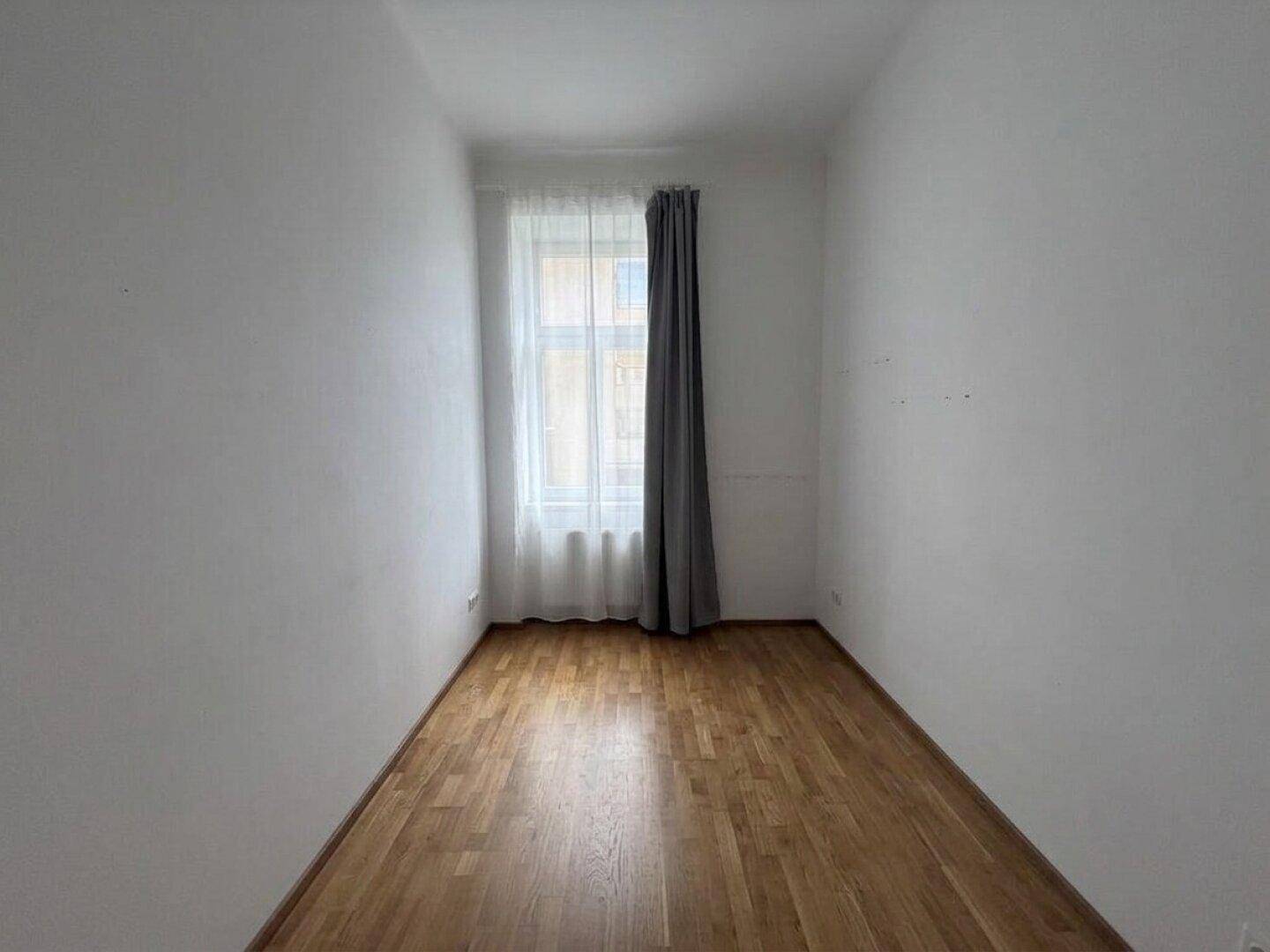 Kleines, helles Zimmer mit Holzboden und einem Fenster, geeignet als Schlaf- oder Arbeitszimmer.