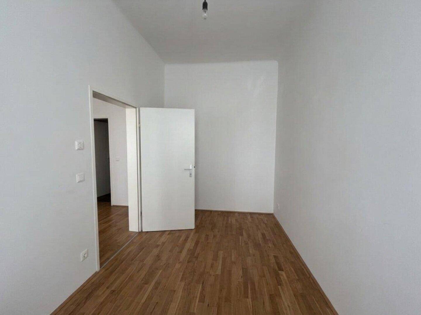 Leeres Zimmer mit Holzboden und weiß gestrichenen Wänden, bietet vielseitige Nutzungsmöglichkeiten.