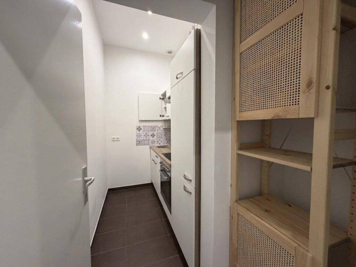 Kompakte Küchenzeile mit weißen Schränken, integrierten Geräten und Holzregalen.