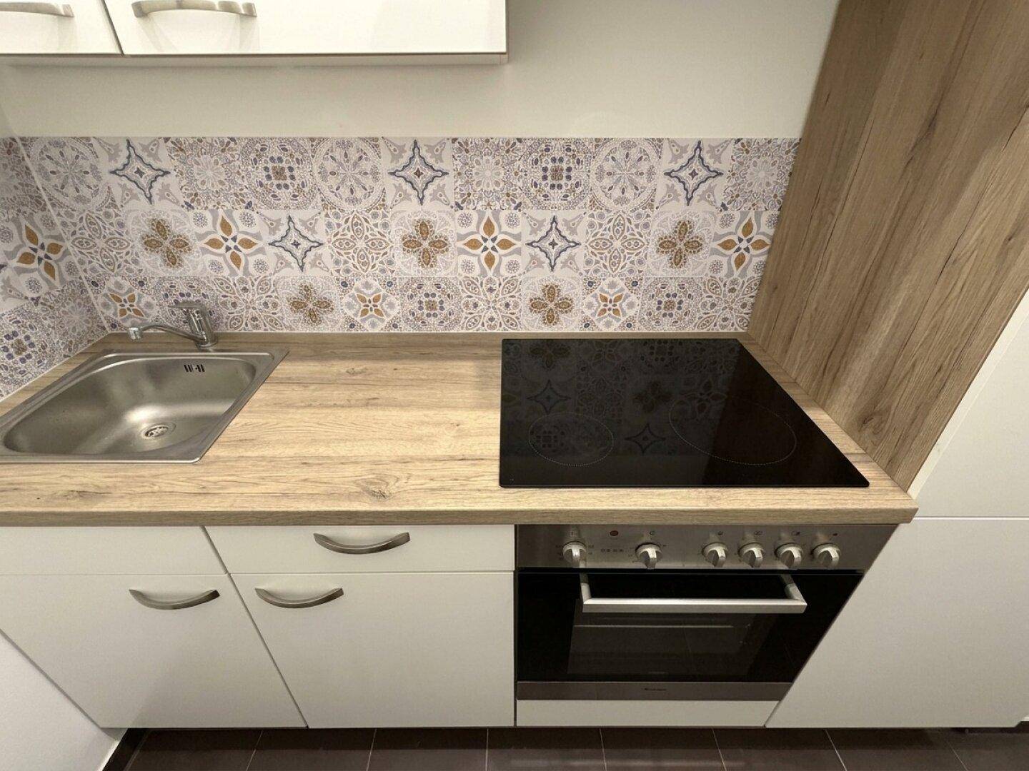 Küchenzeile mit Holz-Arbeitsplatte, Spüle, Induktionskochfeld und dekorativem Fliesenspiegel.