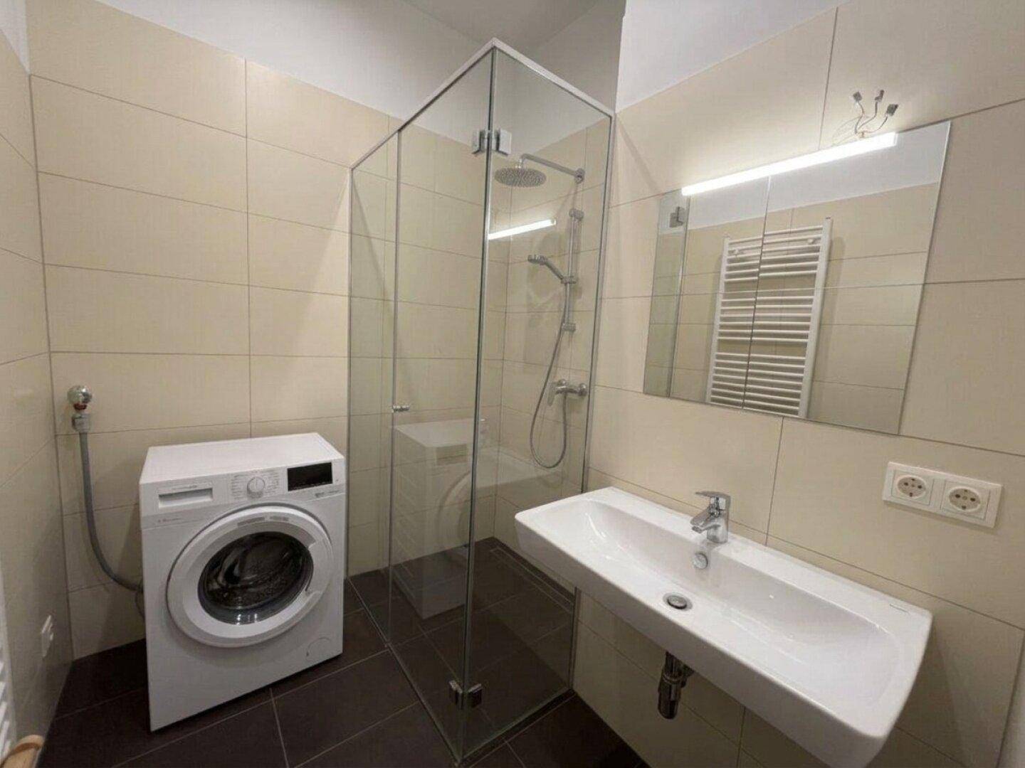 Modernes Badezimmer mit ebenerdiger Glasdusche, Waschmaschine und beheiztem Handtuchhalter.