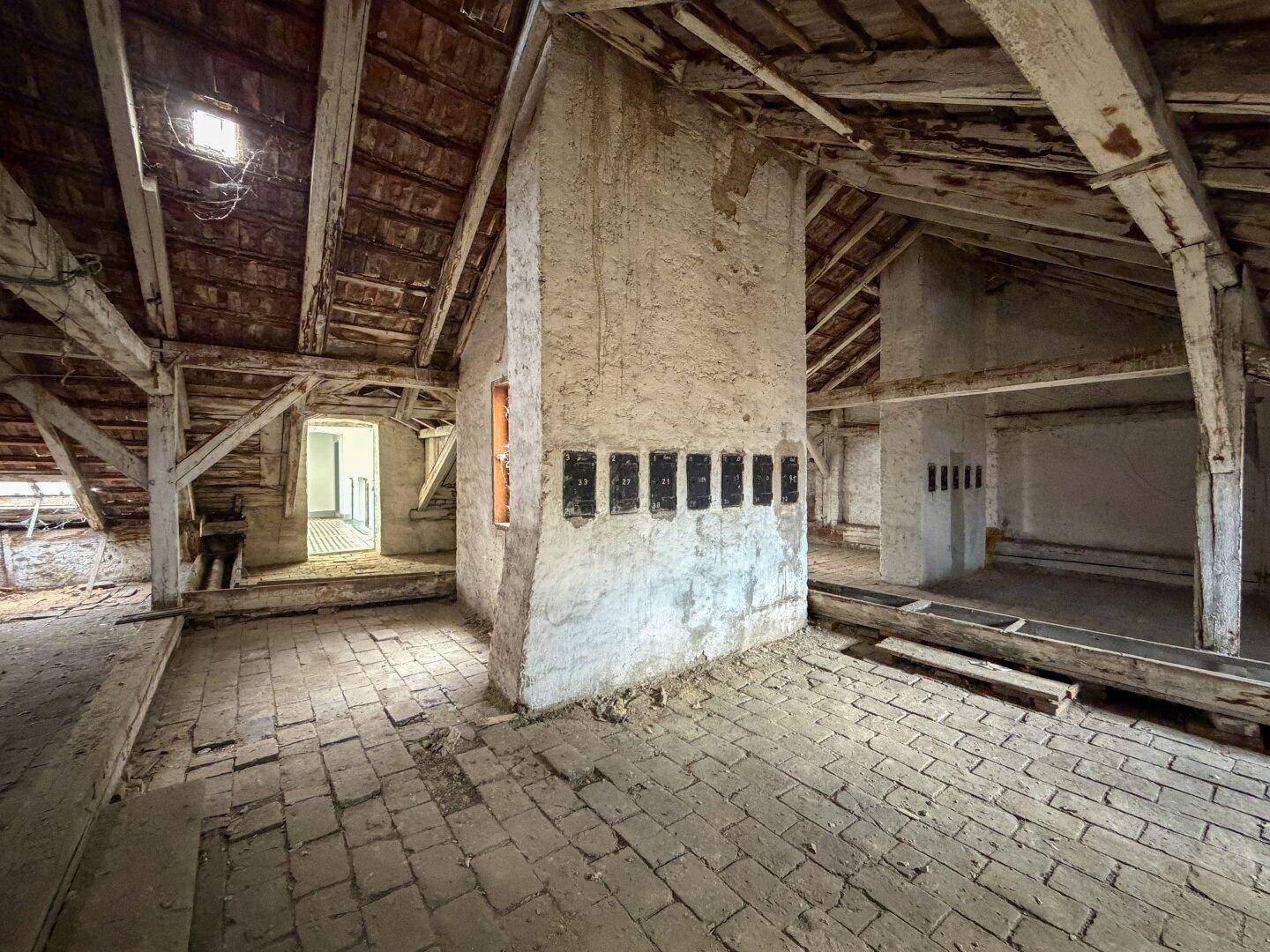 Rustikaler Dachboden mit freiliegenden Holzbalken, Ziegelboden und einem gemauerten Kaminzug.