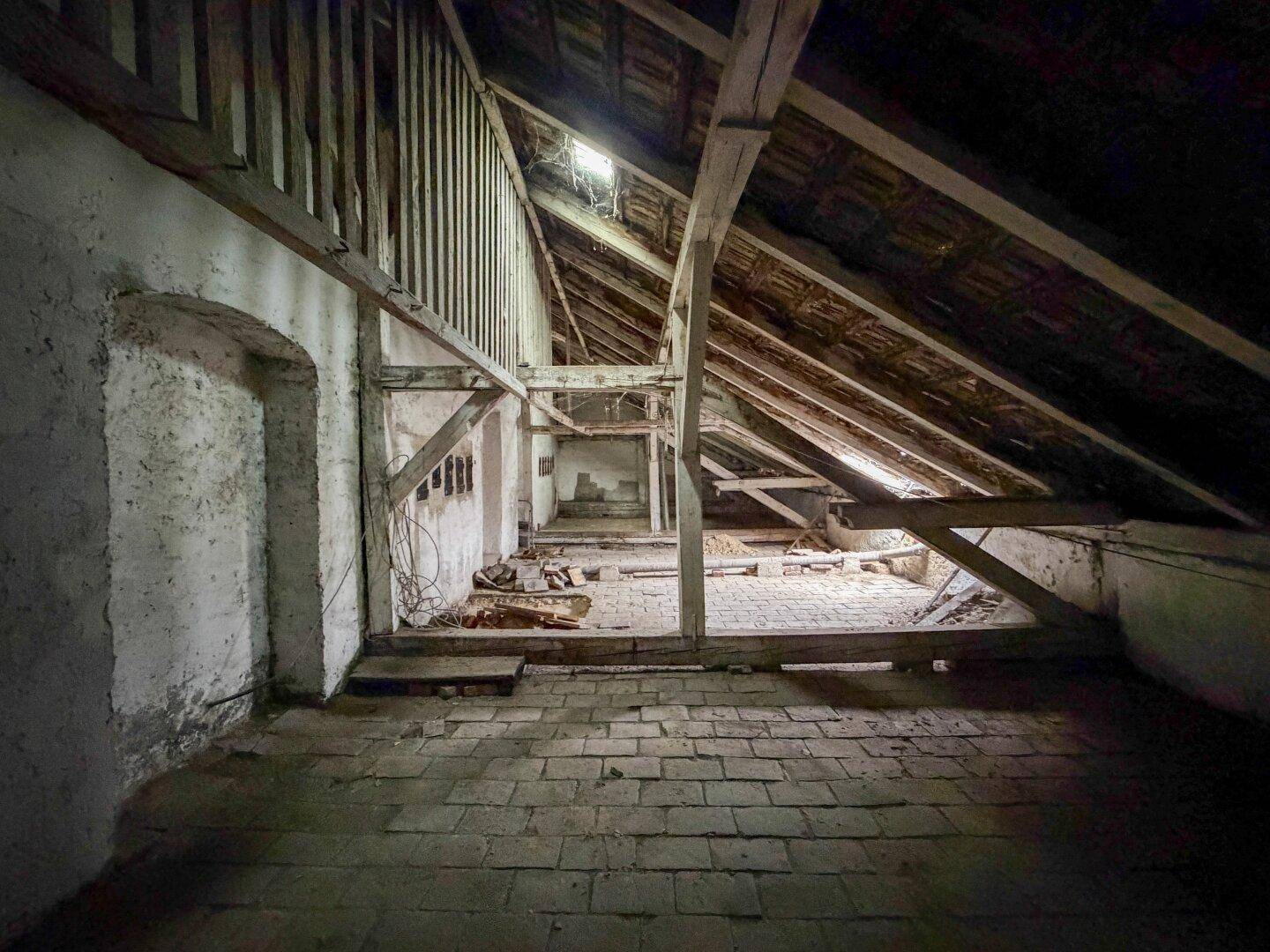 Letzter Blick in den weitläufigen Dachboden mit beeindruckender Holzkonstruktion und Ziegelboden.