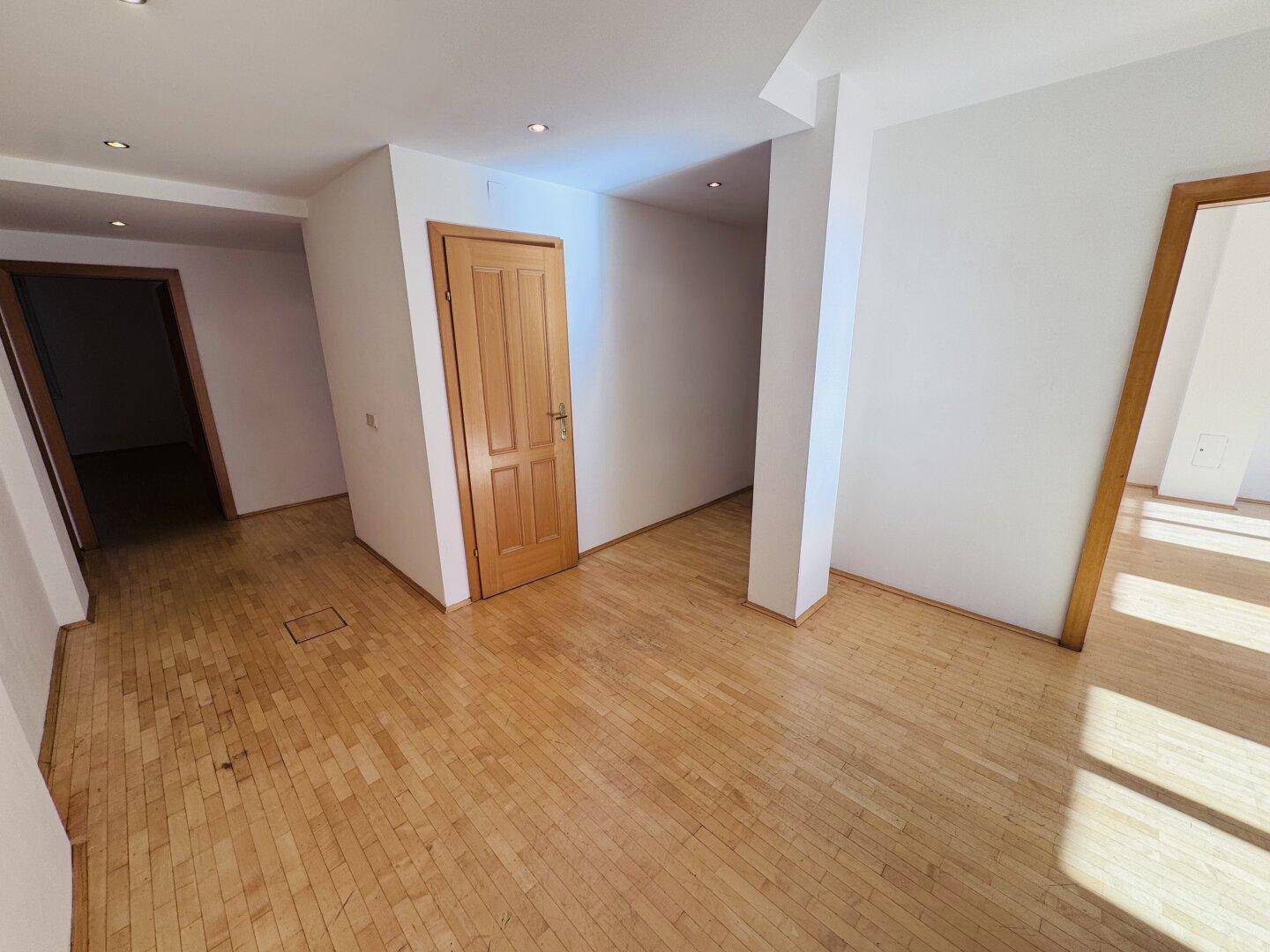 Heller Flur mit Holzboden und mehreren Türen, der verschiedene Räume miteinander verbindet.