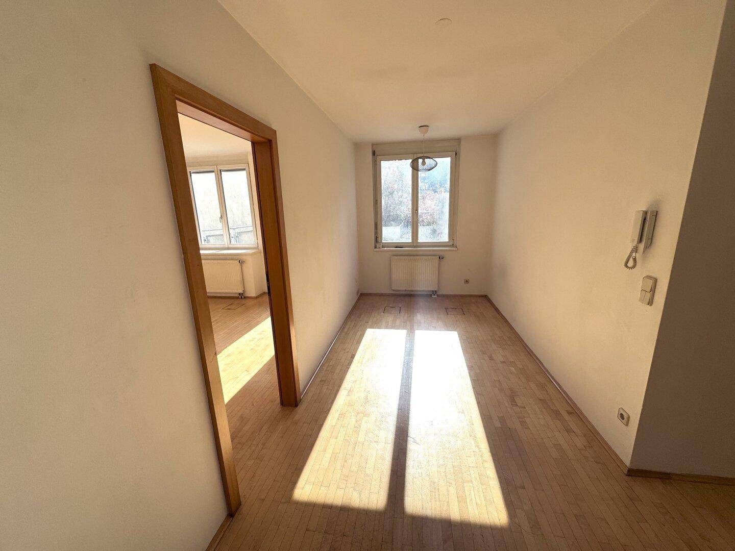 Leerer Raum mit Holzboden und einem Fenster, das viel natürliches Licht hereinlässt.