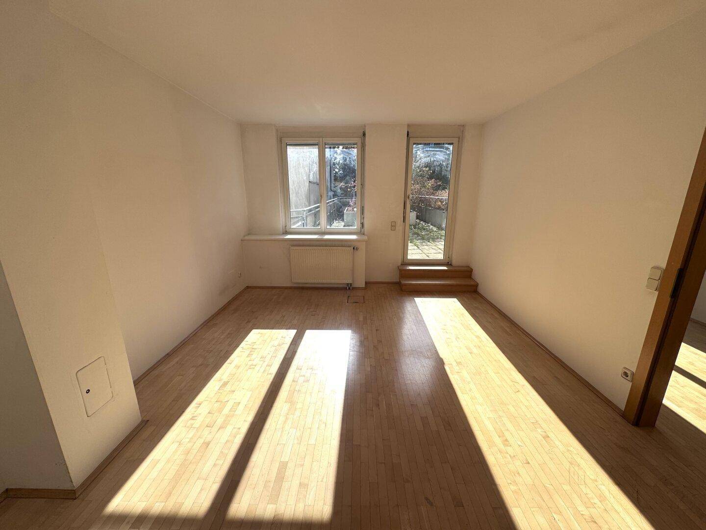 Heller Raum mit Holzboden und Zugang zu einem Außenbereich durch eine Tür.