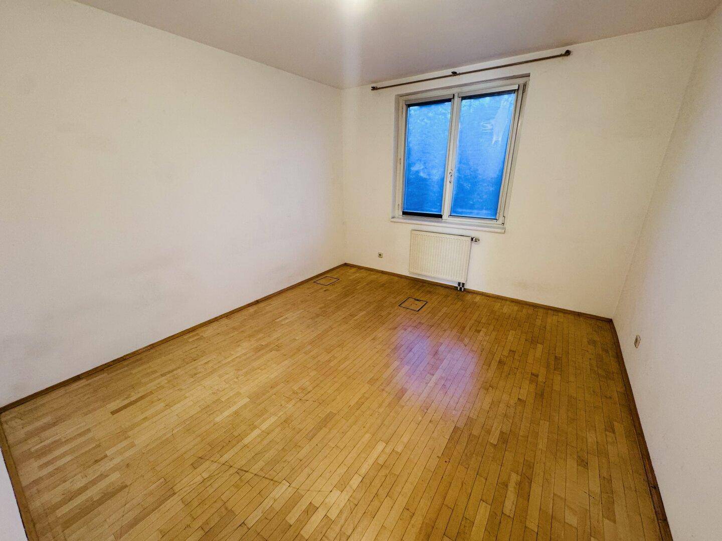 Leerer Raum mit Holzboden und einem Fenster, das den Raum mit Tageslicht versorgt.
