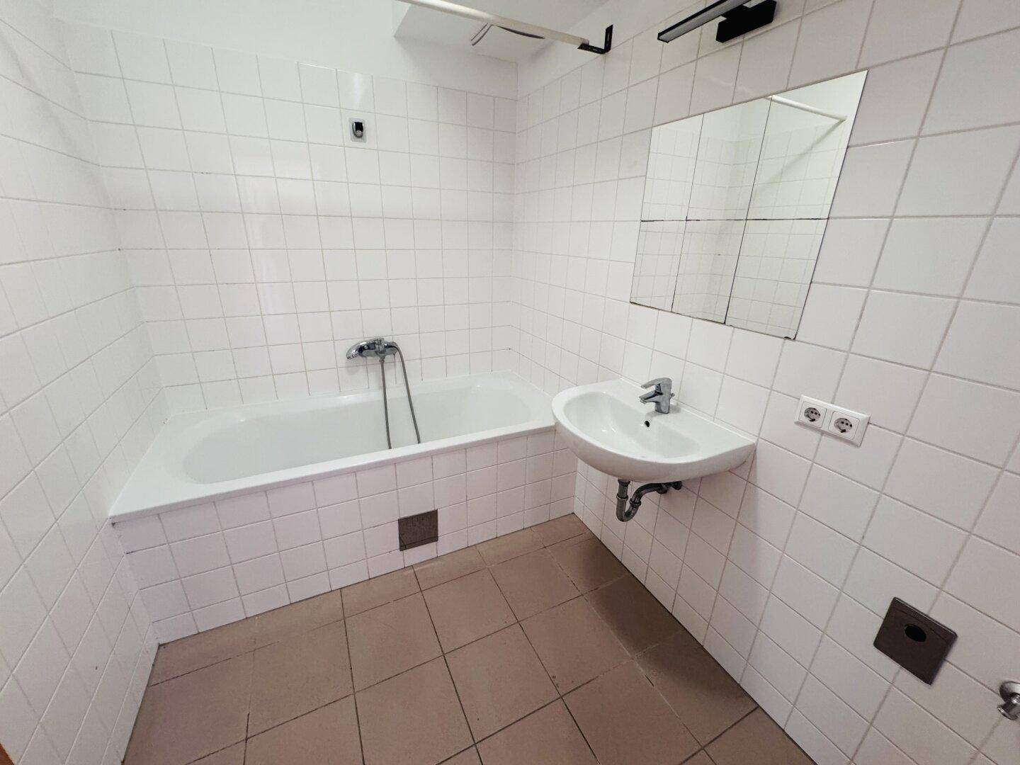 Badezimmer mit weißen Fliesen, Badewanne, Waschbecken und einem Spiegel.