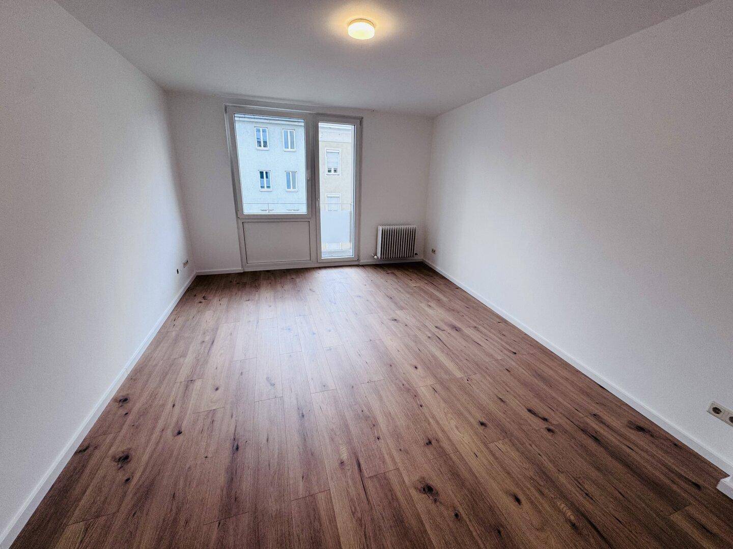 Heller Raum mit Laminatboden, weißen Wänden und Zugang zu einem Außenbereich.