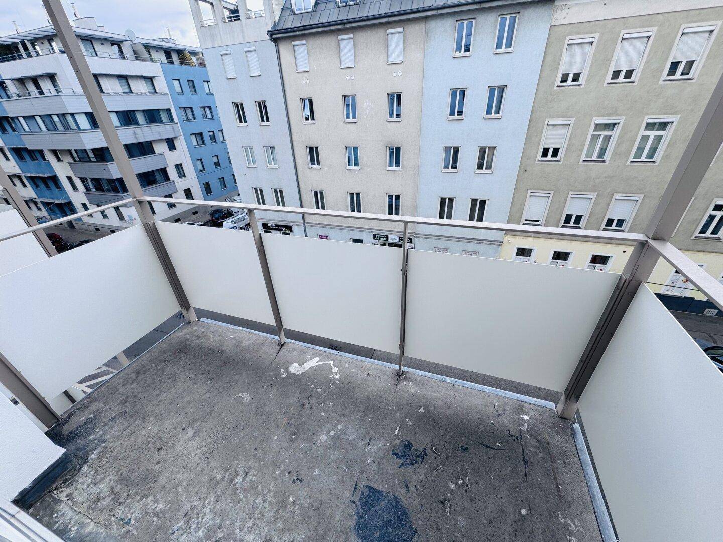 Unmöblierter Balkon mit Betonboden und Blick auf die umliegenden Stadtgebäude.