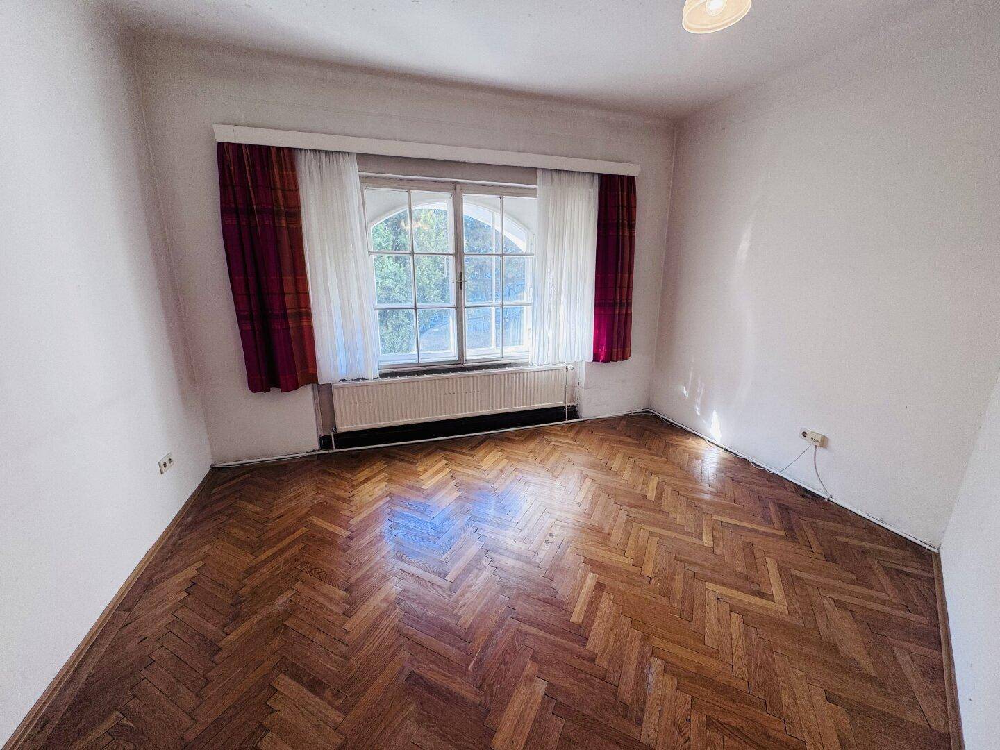 Kleineres Zimmer mit Fischgrätparkett und einem Fenster, ideal als Schlaf- oder Arbeitszimmer.