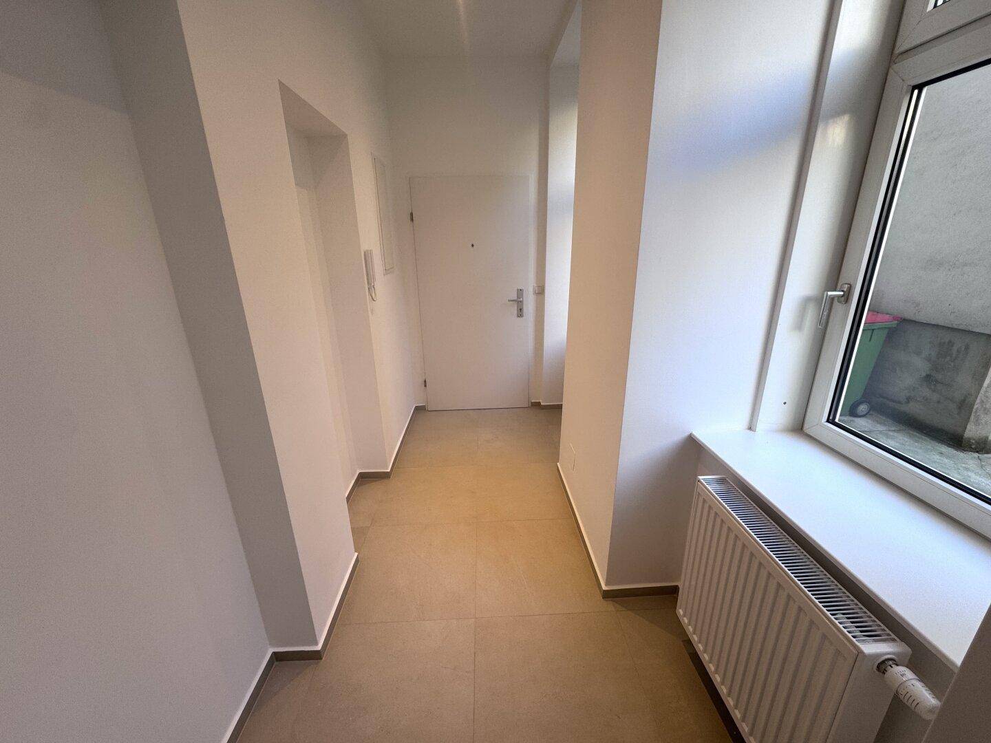 Heller Flur mit Fliesenboden und einer Eingangstür, der den Zugang zur Wohnung ermöglicht.