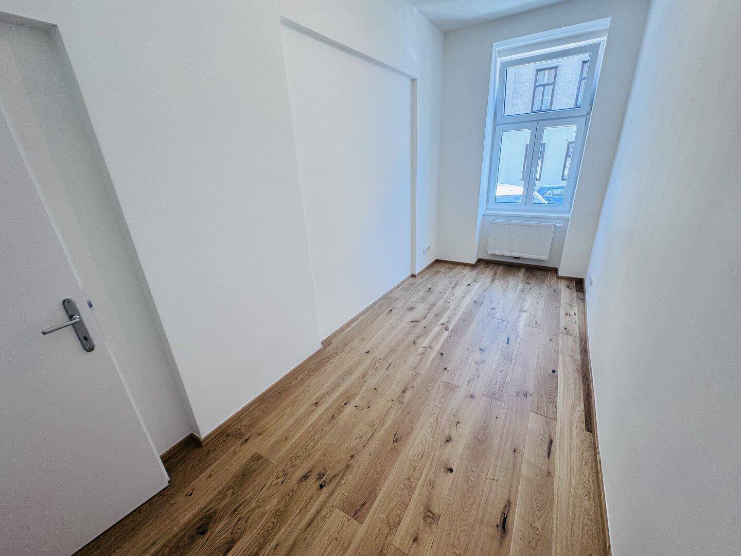 Helles Zimmer mit Holzboden und einem Fenster, das viel Tageslicht in den Raum bringt.