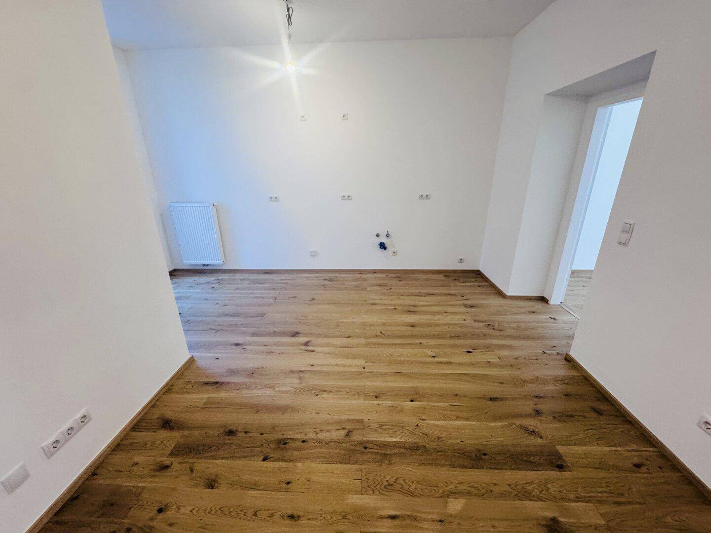 Heller Raum, vorbereitet für eine Küche, mit Holzboden und Anschlüssen für Geräte.