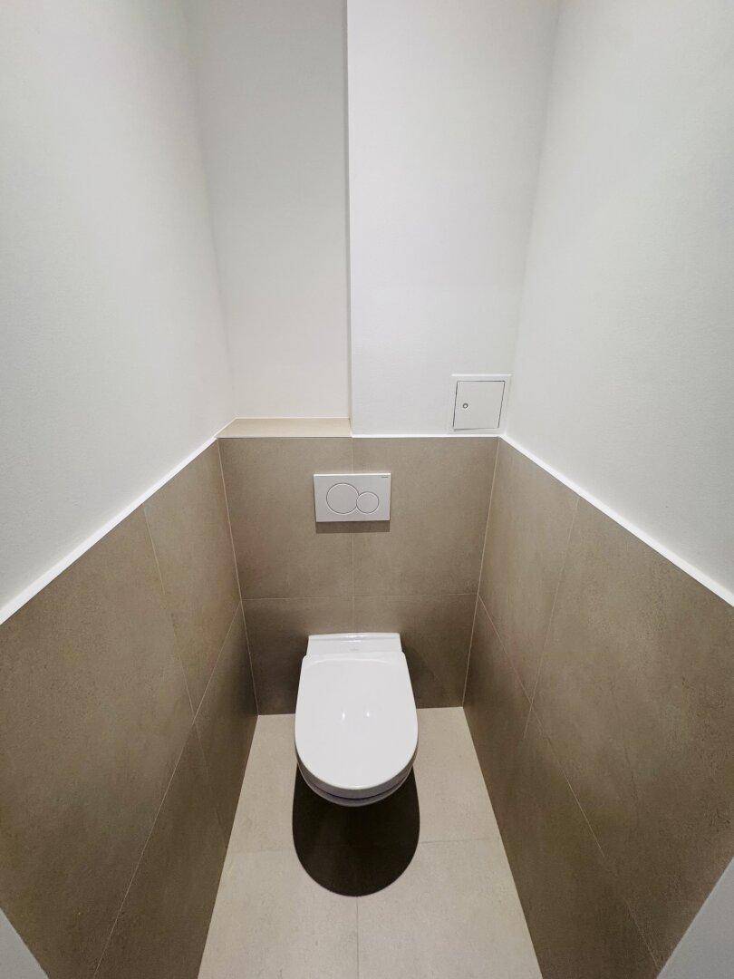 Modernes Gäste-WC mit Wand-WC und beigefarbenen Fliesen an Wänden und Boden.