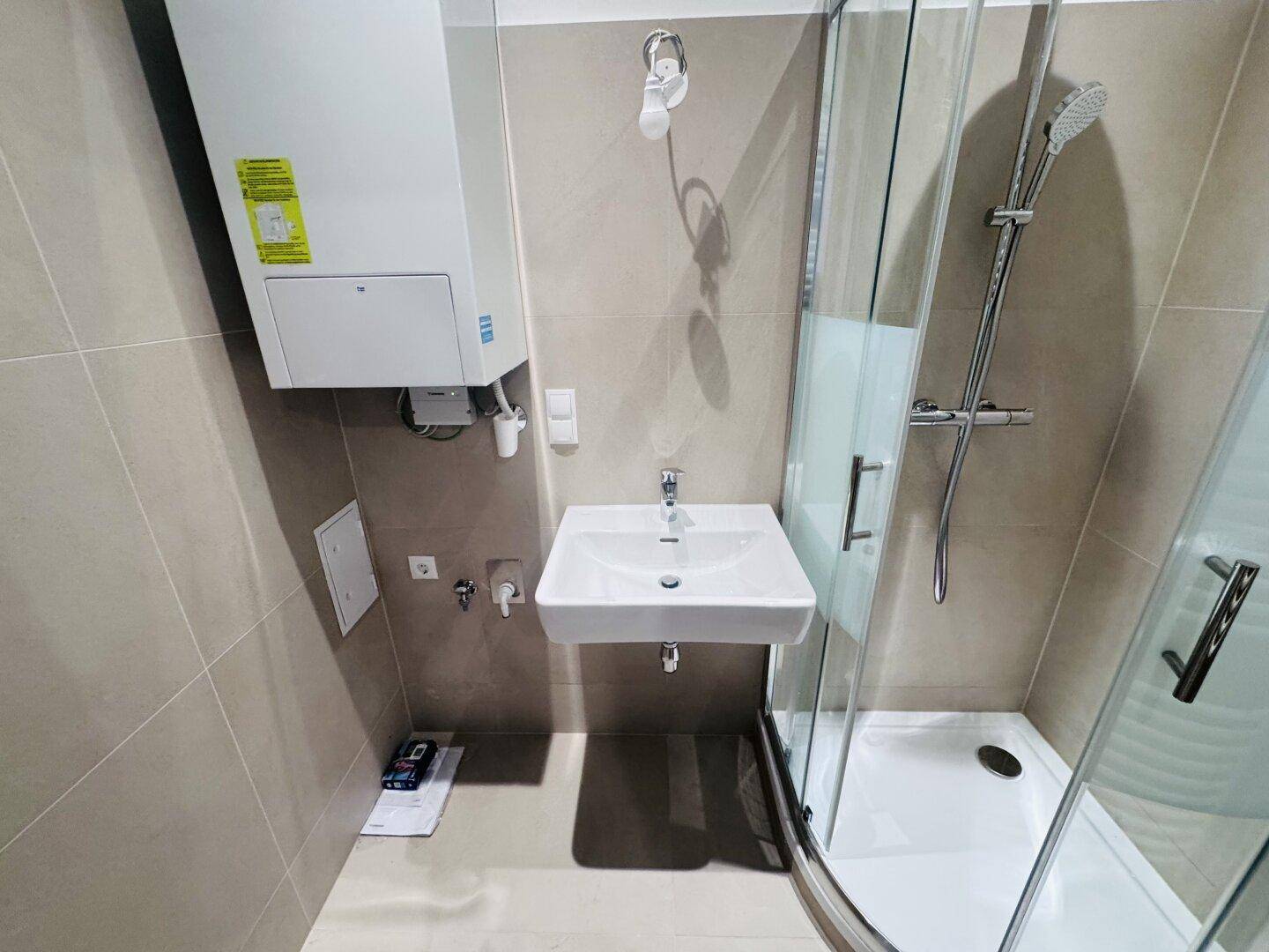 Modernes Badezimmer mit Dusche, Waschbecken und beigefarbenen Fliesen, inklusive Warmwasserbereiter.