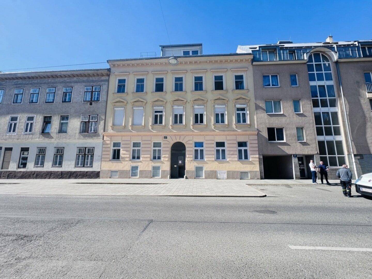 Historisches Gebäude mit klassischer Fassade und mehreren Fenstern an einer städtischen Straße.