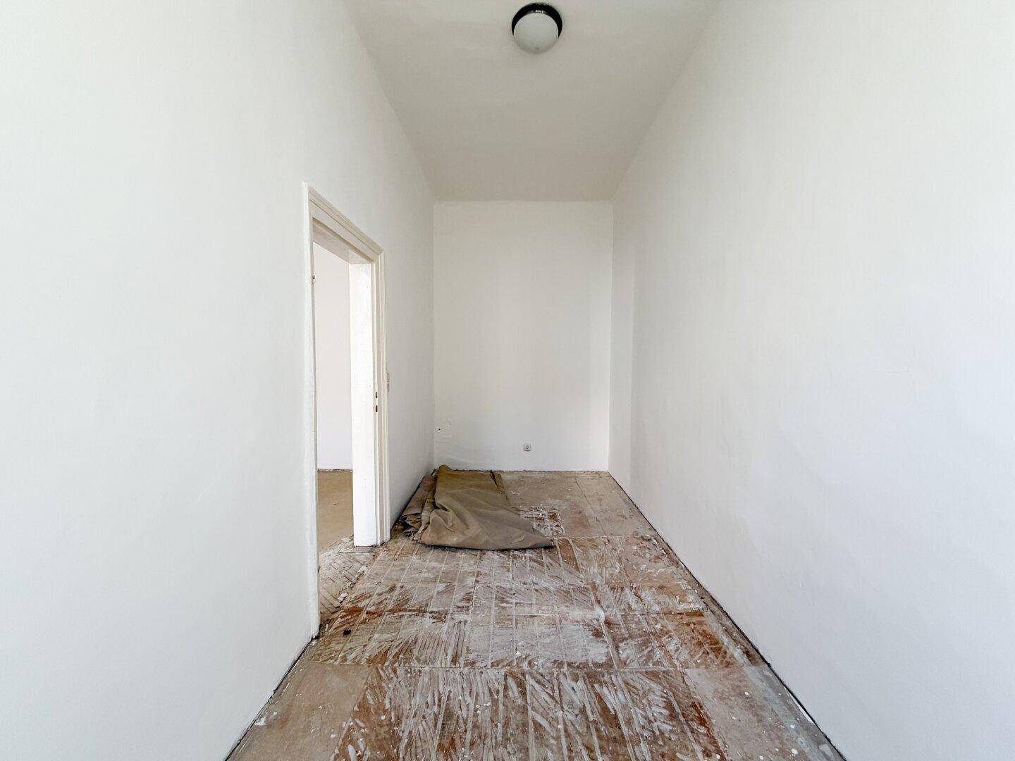 Langer, leerer Raum mit alten Holzdielen und einer Deckenleuchte, bereit zur Umgestaltung.