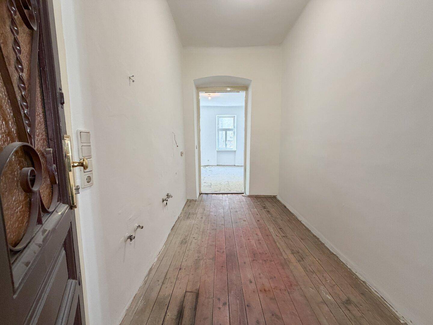 Eingangsbereich mit einer verzierten Holztür und alten Dielen, der in die Wohnung führt.