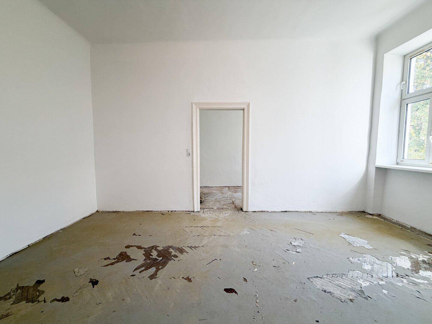 Heller, leerer Raum mit einem Fenster und stark beschädigtem Boden, ideal für eine Neugestaltung.