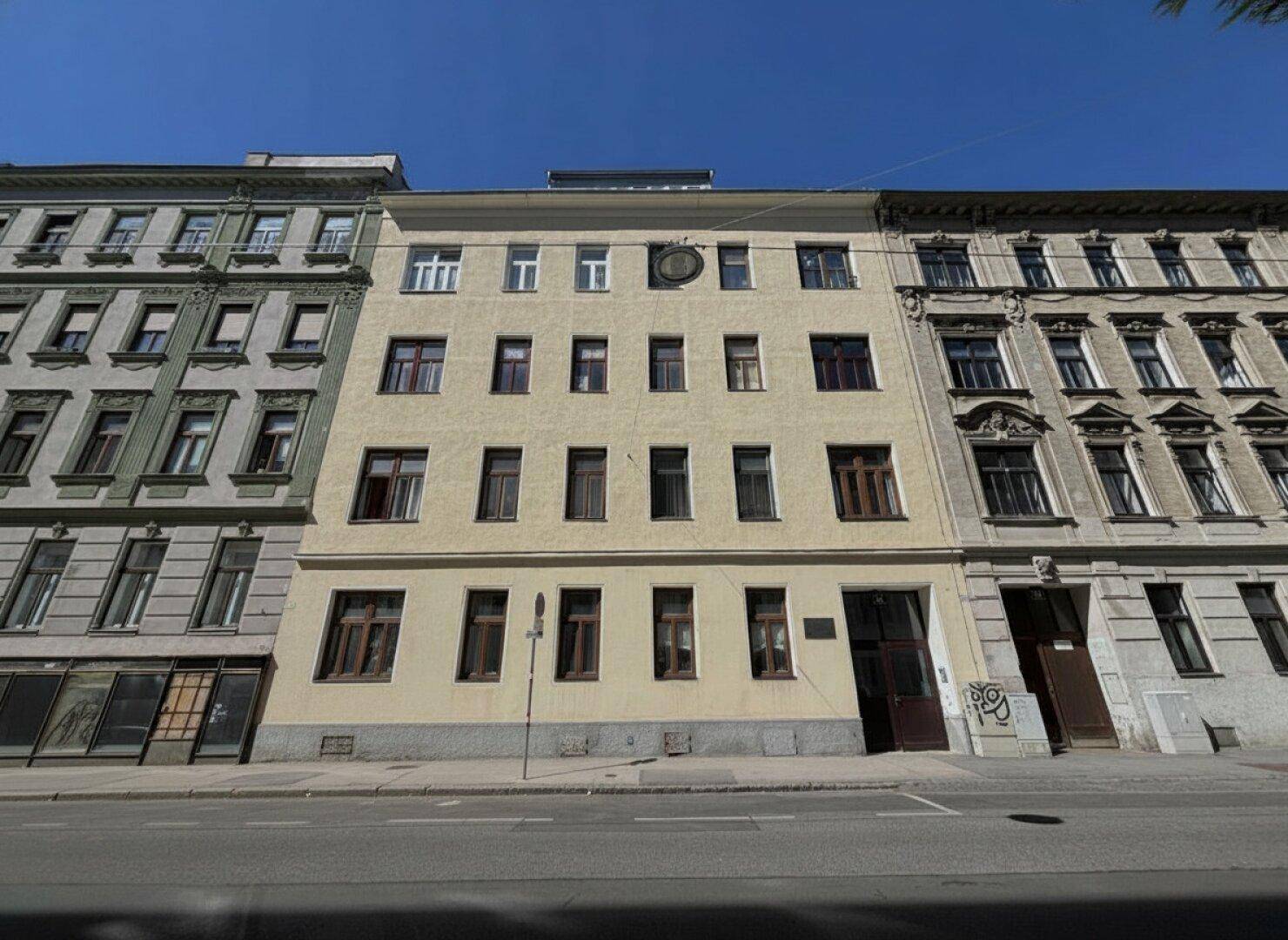 Historische Fassade eines Mehrfamilienhauses an einer Stadtstraße mit vielen Fenstern.
