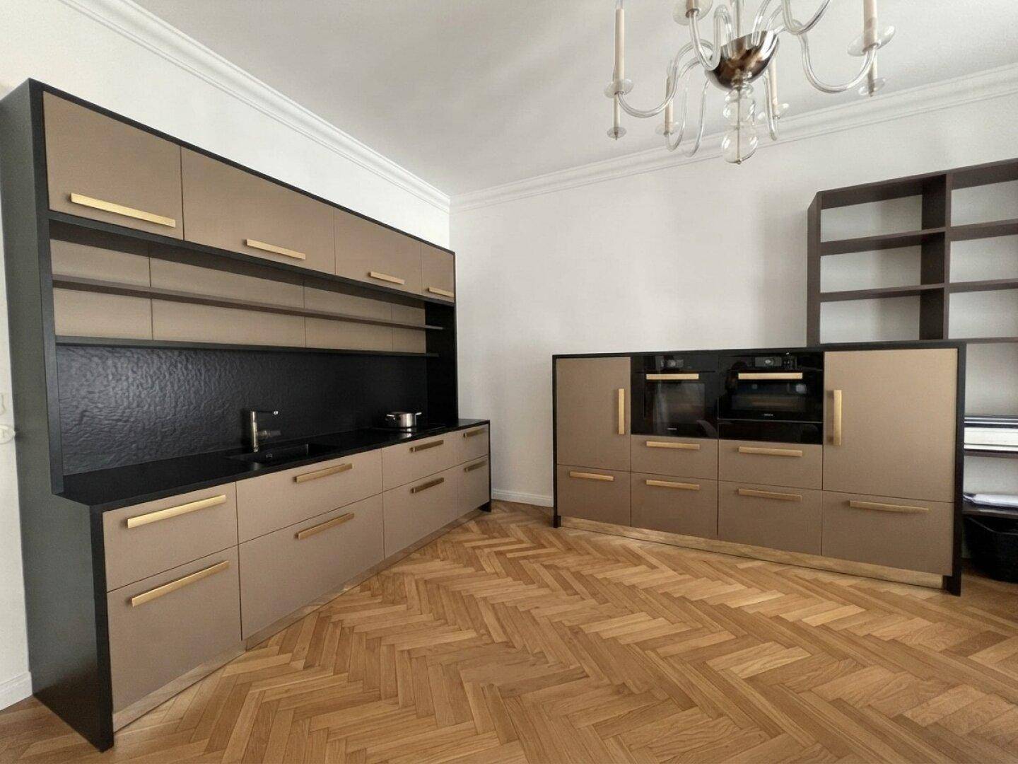 Moderne Küche mit beigen Schränken, schwarzen Arbeitsplatten und Parkettboden.